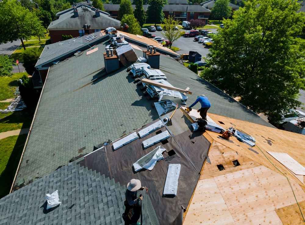 Roofers repairing a shingled roof, with materials spread across the rooftop