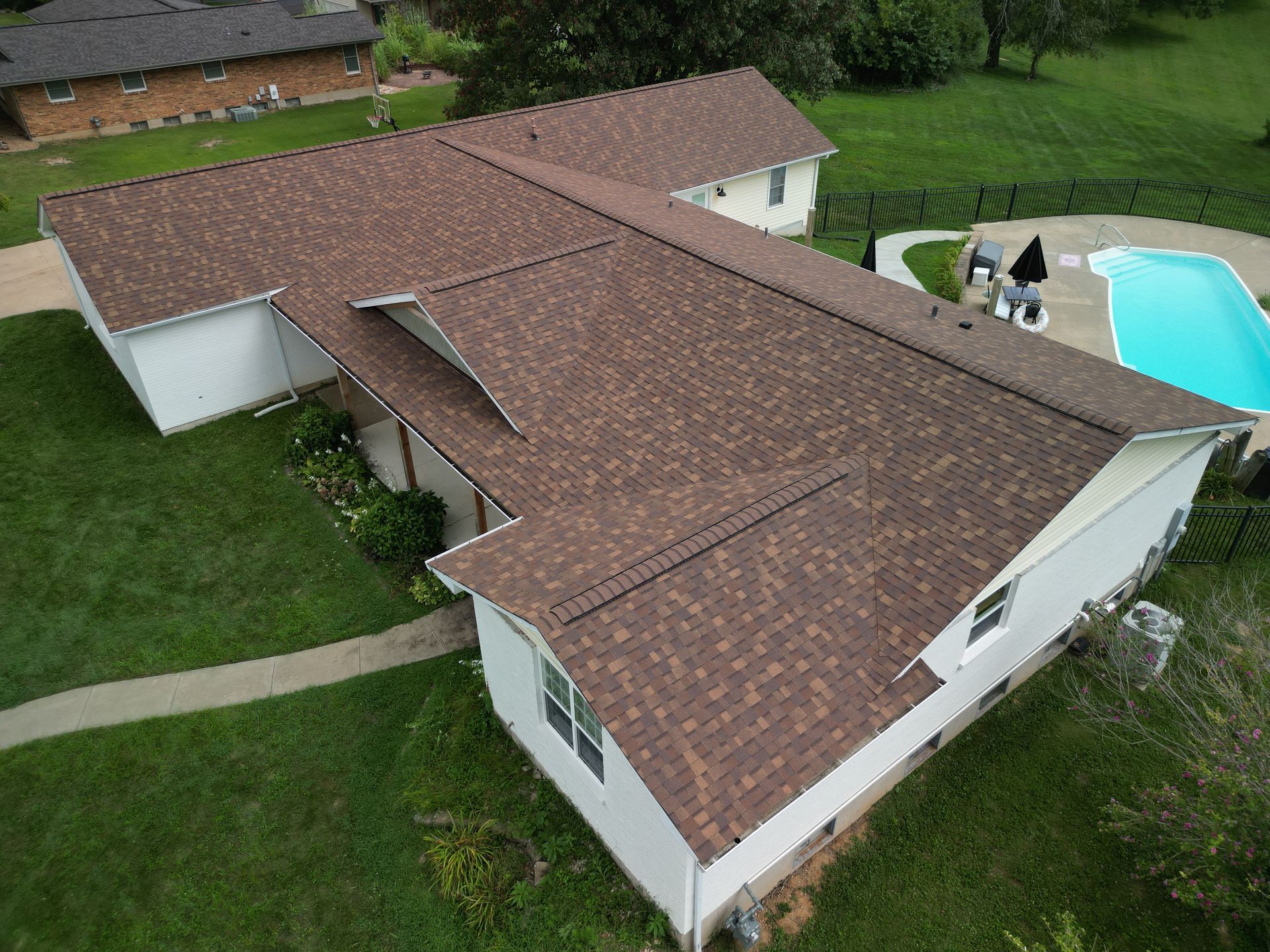 Aerial view of a large house with a brown roof, green lawn, and backyard swimming pool.