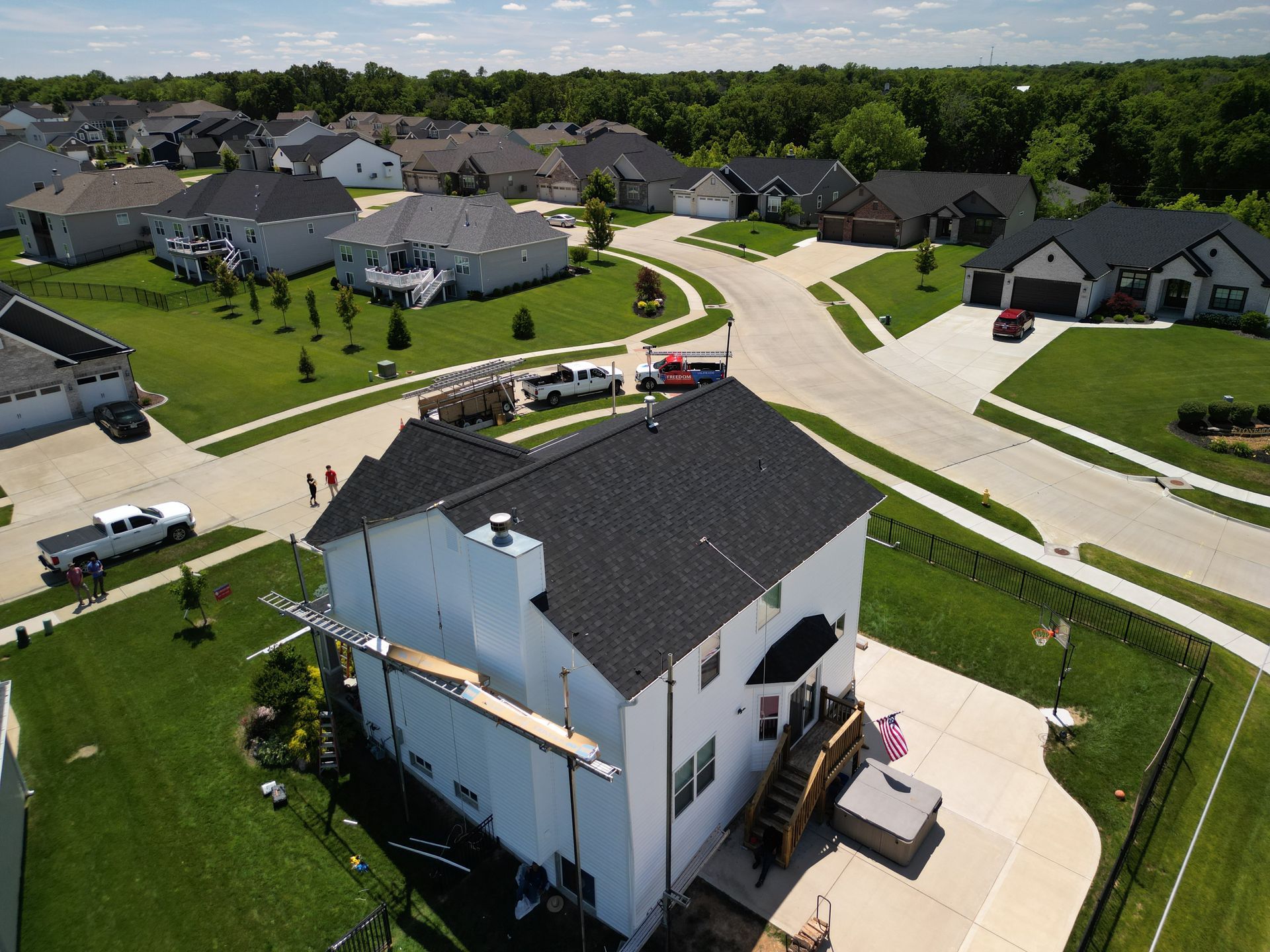 Aerial view of a suburban neighborhood with a white house in the foreground and curved streets beyond.