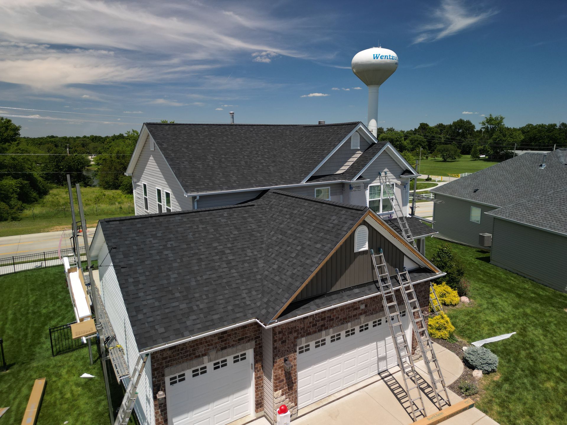 Aerial view of a suburban house with a dark roof, attached garage, and a water tower in the background
