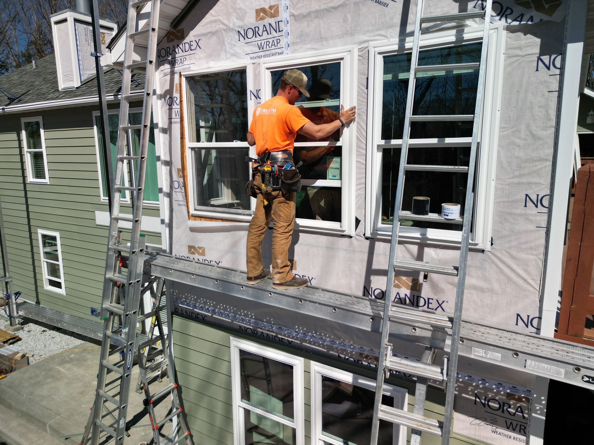 Construction worker installing siding on a house from a ladder beside scaffolding