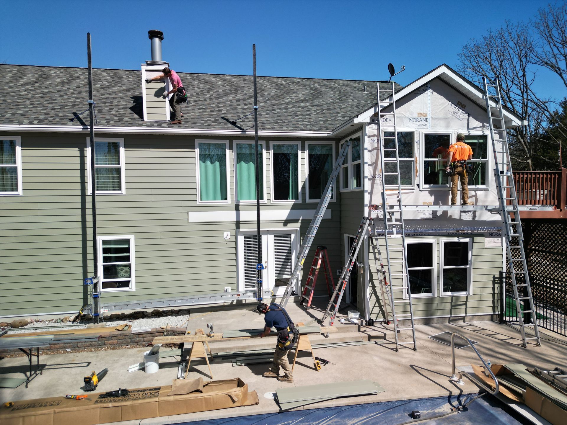 House exterior under renovation with workers on scaffolding and debris in the yard