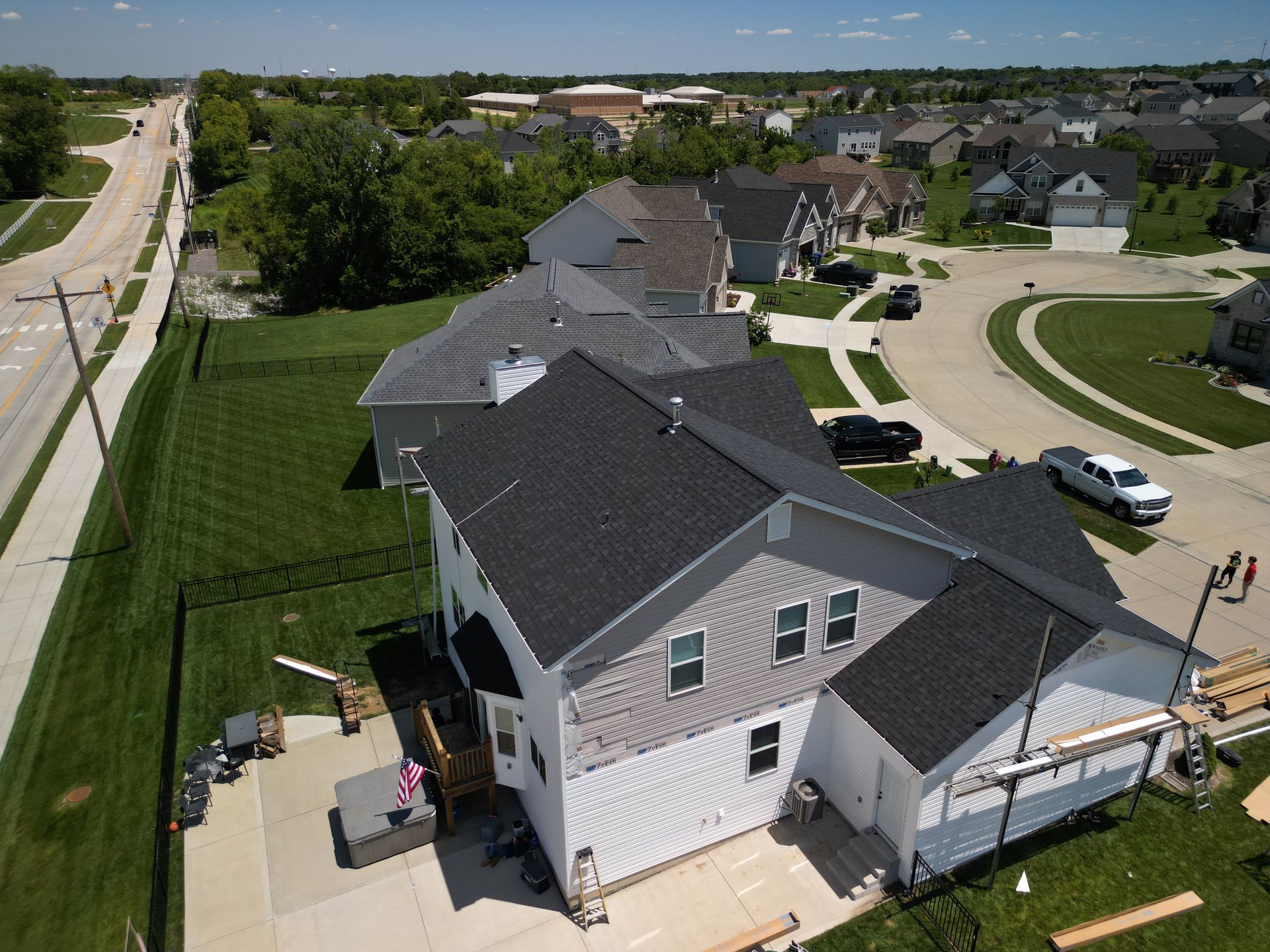 Aerial view of a suburban house with a fenced yard beside a curved street and sidewalk.