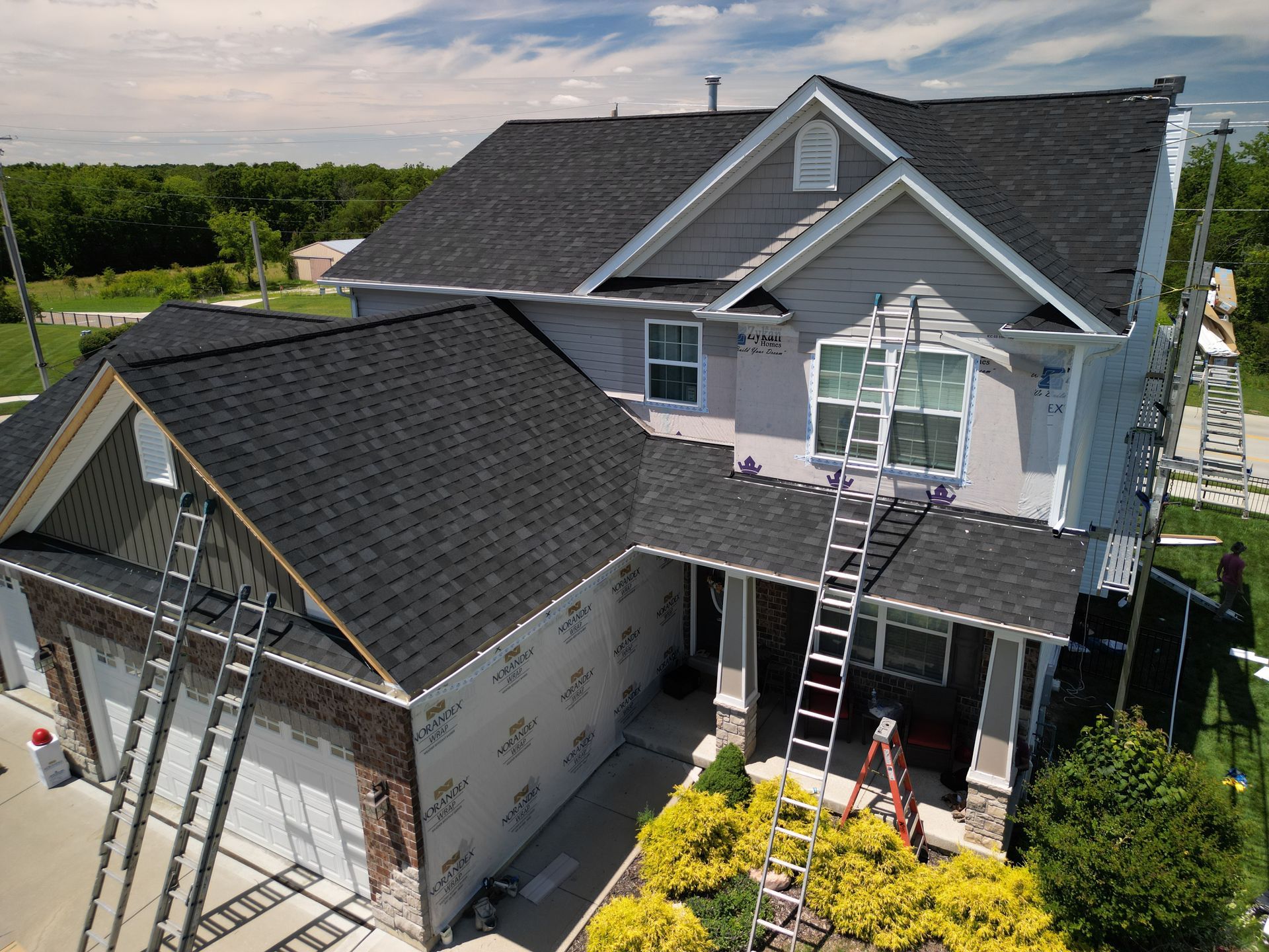 Two workers on ladders repairing a gray house roof and siding above a front porch.