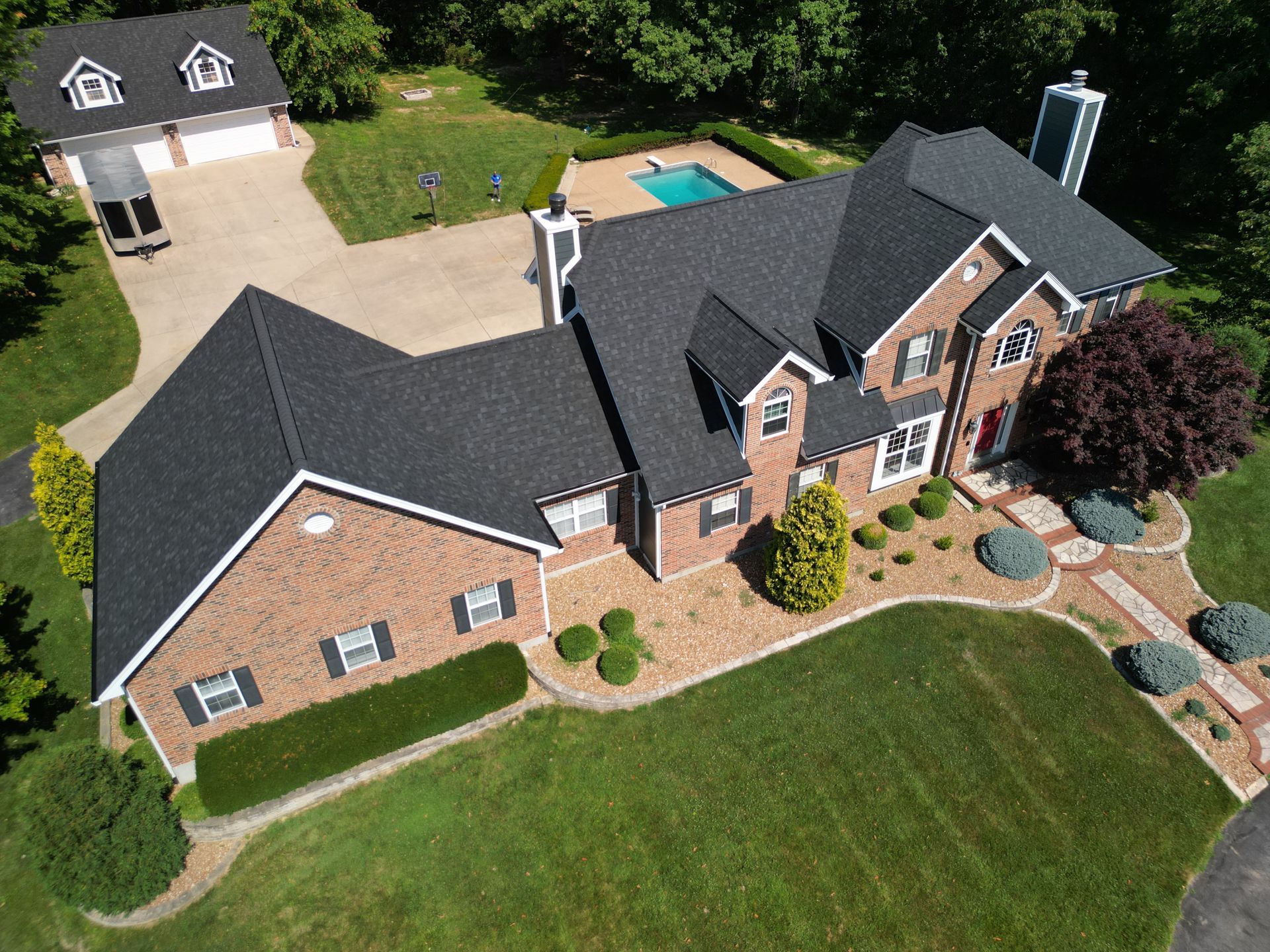 Aerial view of a large brick suburban house with a manicured lawn, curved walkway, and backyard pool