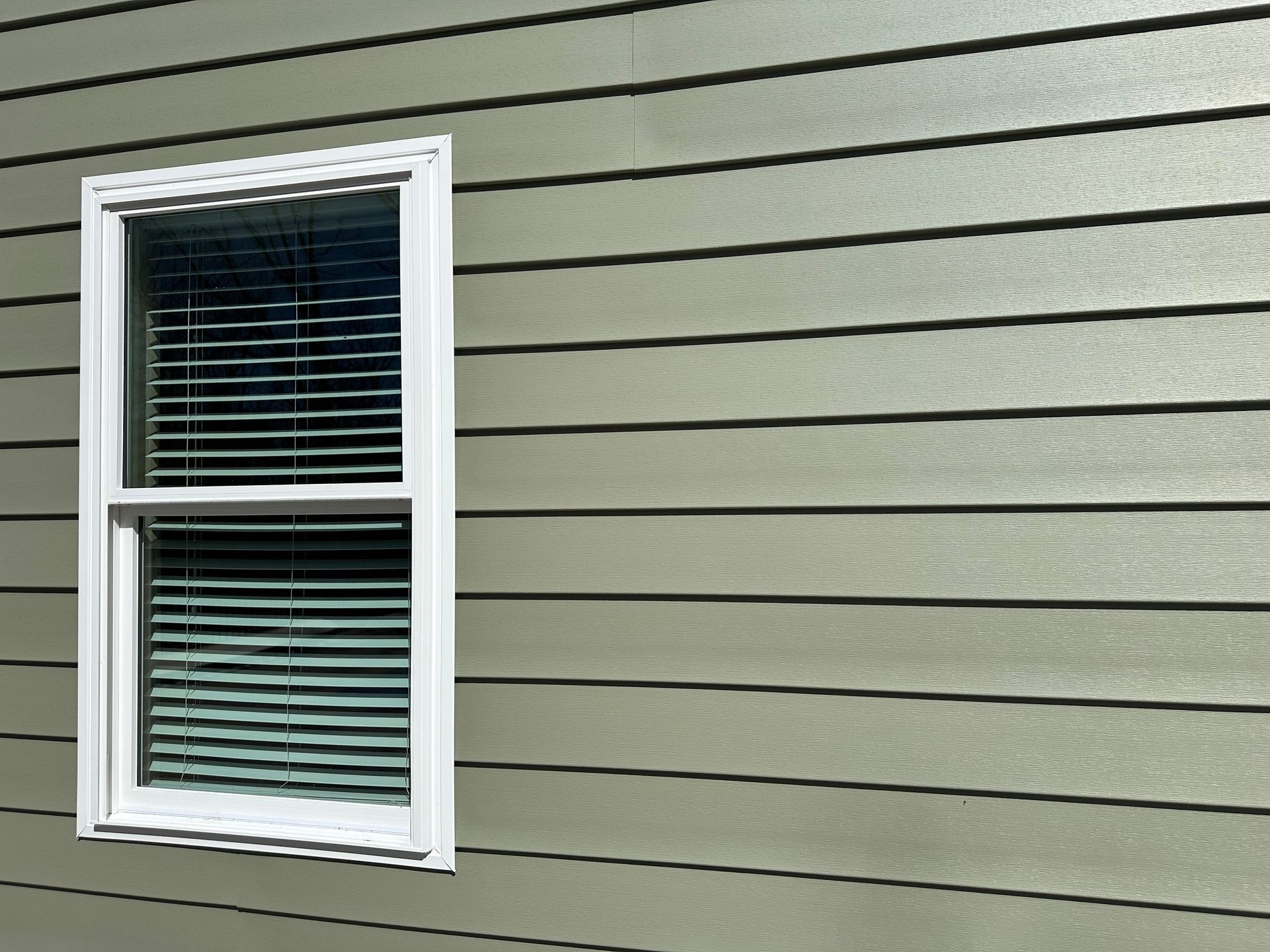 White-framed window with closed blinds on a beige house exterior