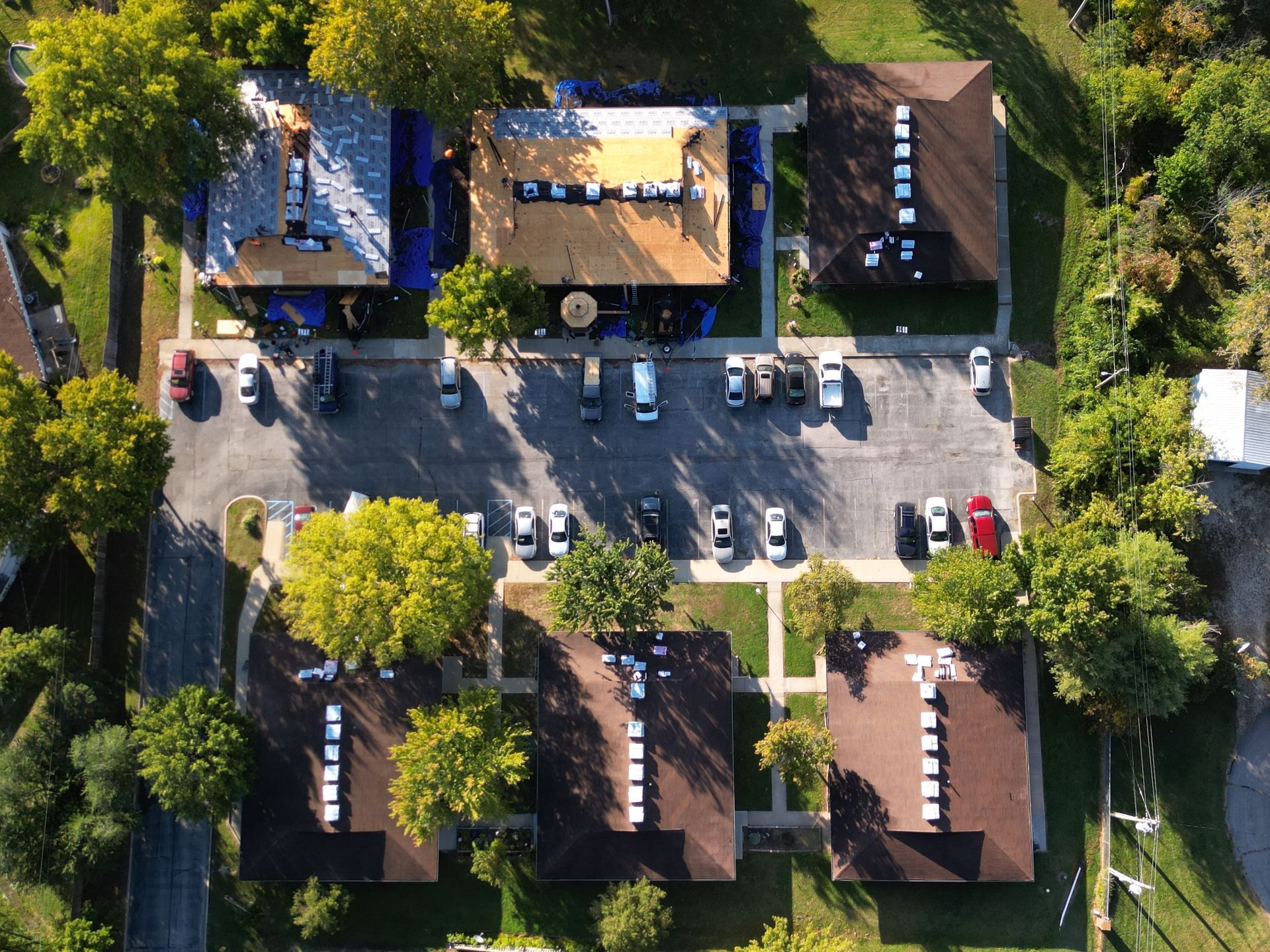 Aerial view of a parking lot beside rooftops and trees, with several parked cars and trucks.