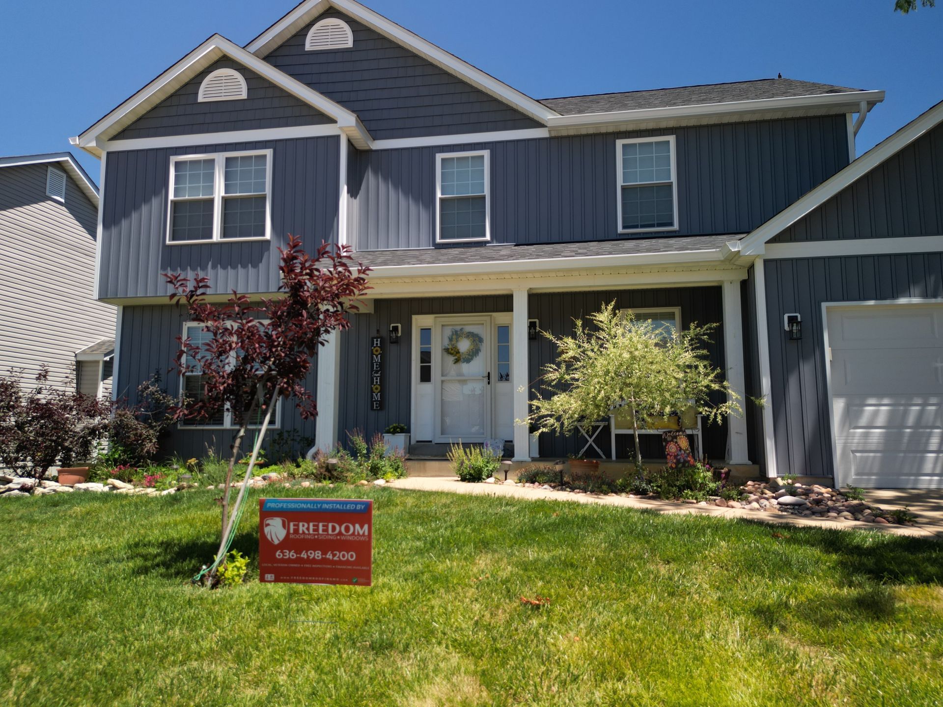 Two-story blue house with white trim and a red sign on a green front lawn