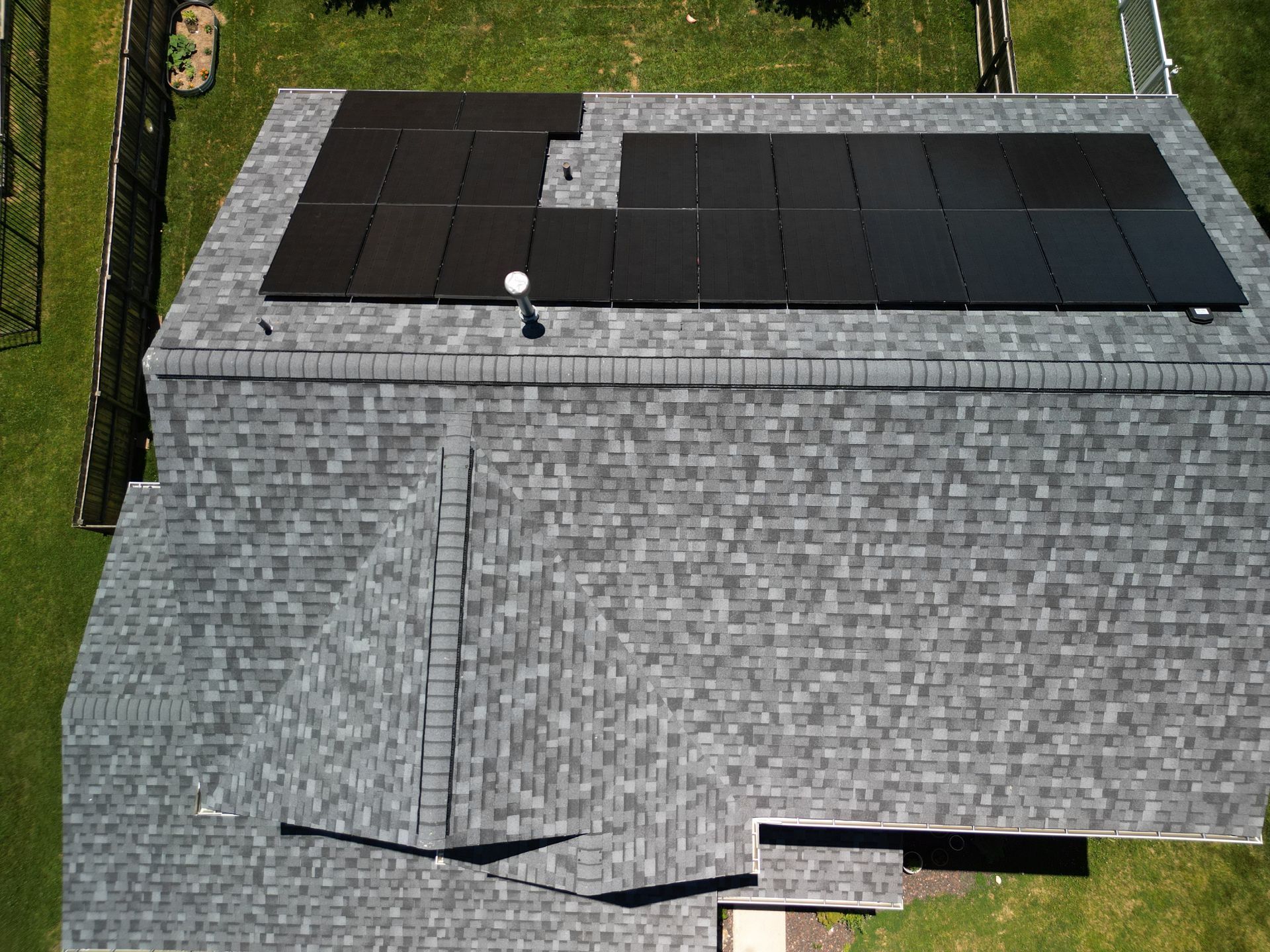 Gray roof with black solar panels on a building, seen from above.