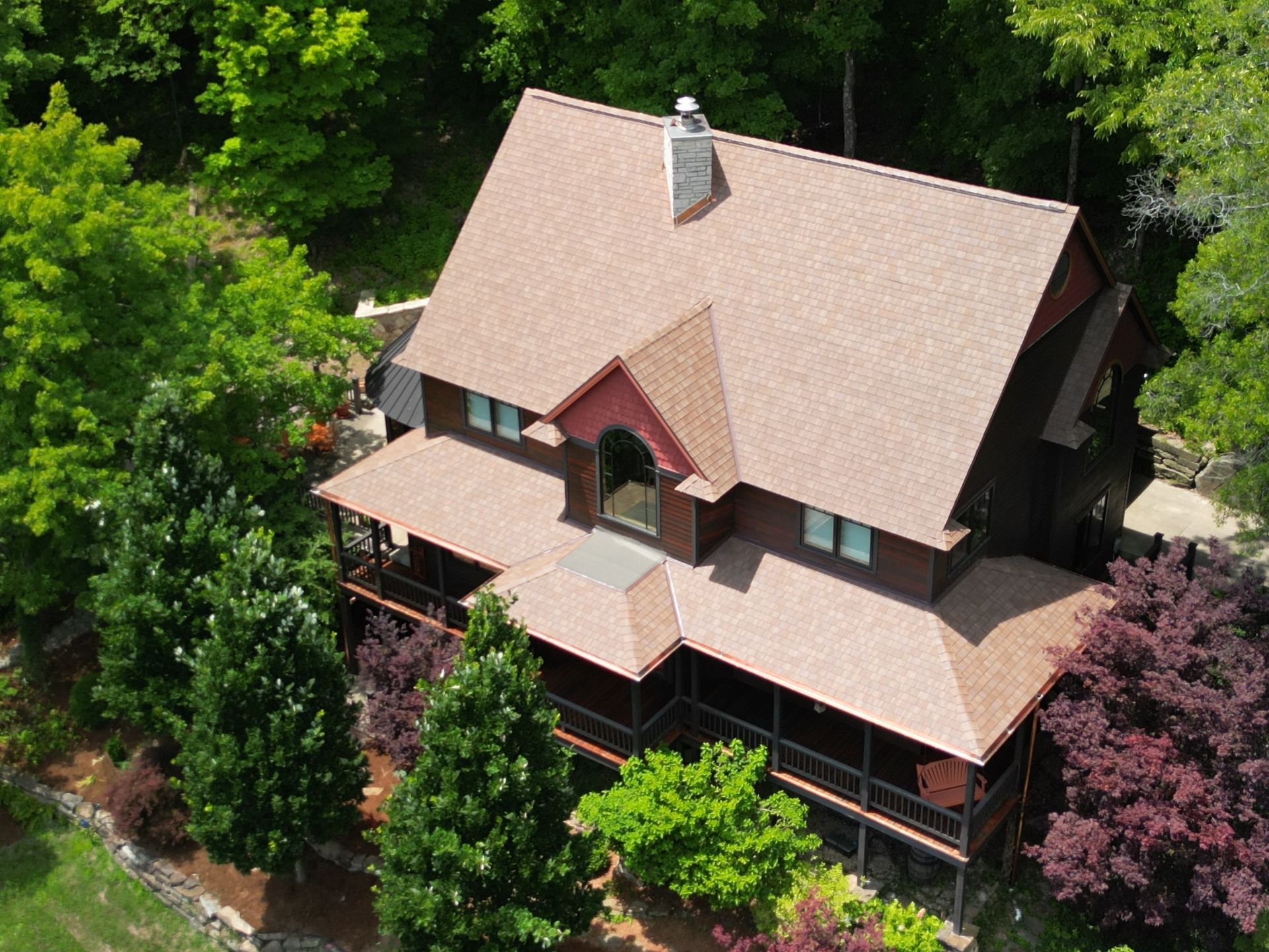 Aerial view of a large house with a brown roof surrounded by lush green trees.