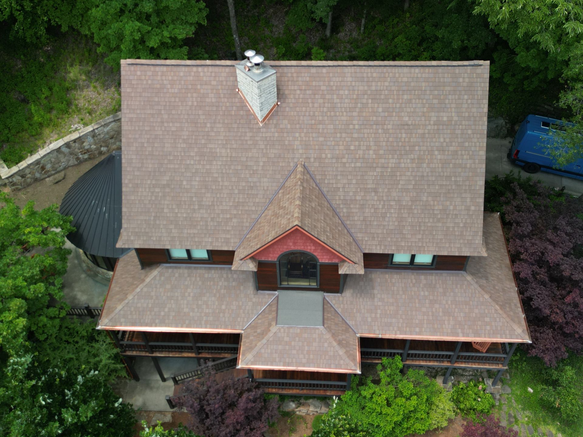 Aerial view of a house with a brown roof, red front gable, and surrounding trees