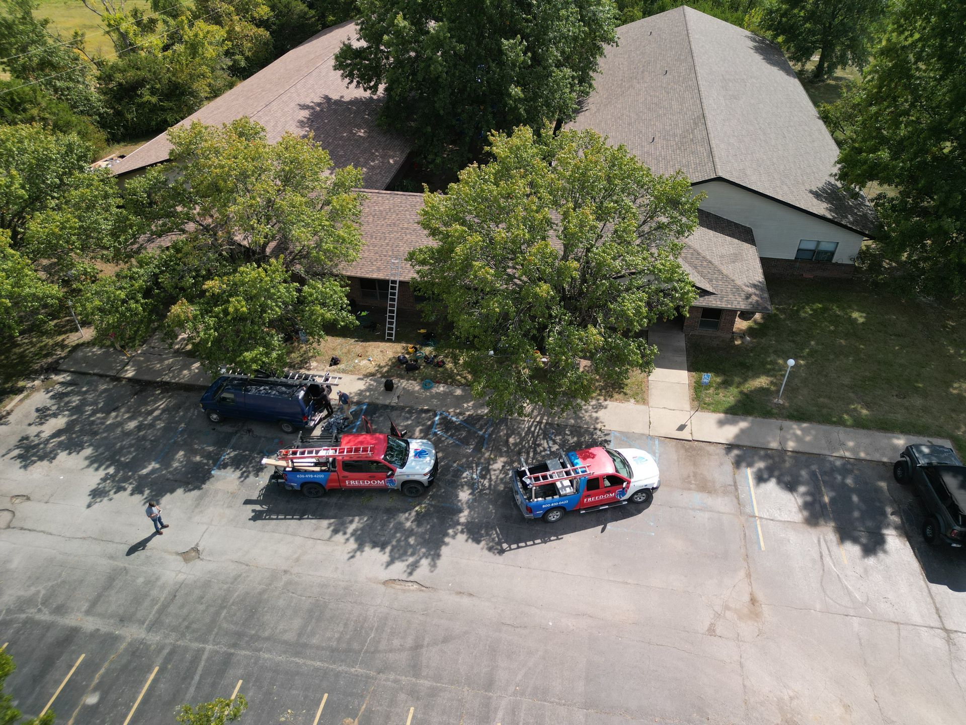 Aerial view of two tow trucks parked on a street beside a tree-shaded house.