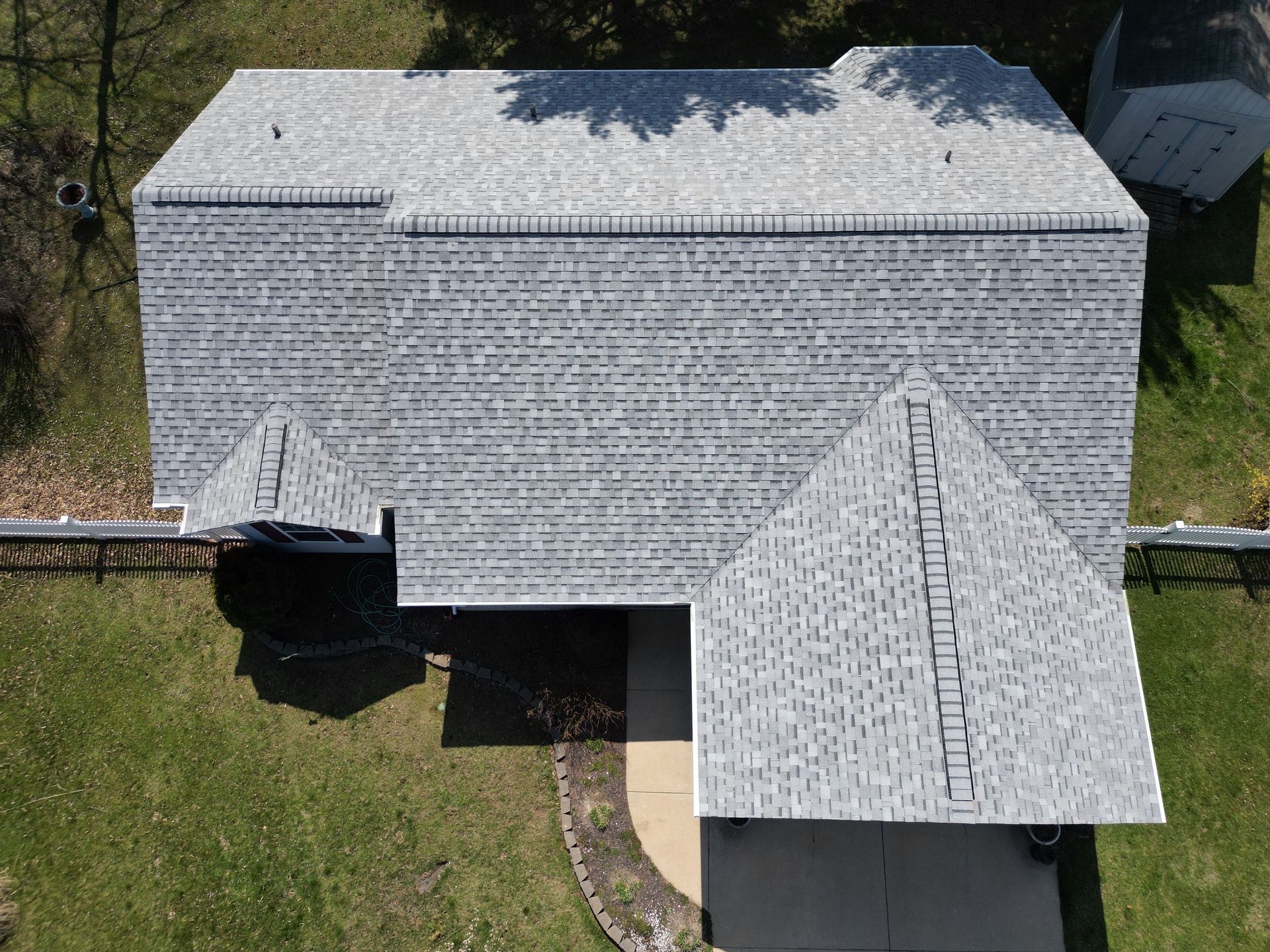 Aerial view of a gray-shingled house roof with a front porch and surrounding trees.