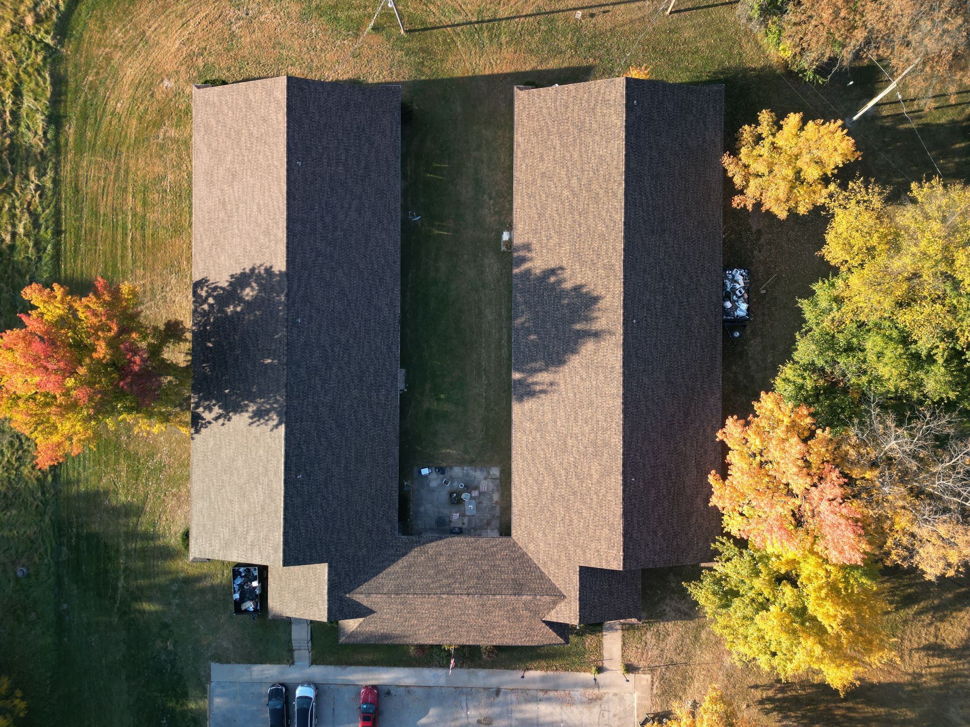 Aerial view of a house with a gray roof, surrounded by green lawn and autumn-colored trees.
