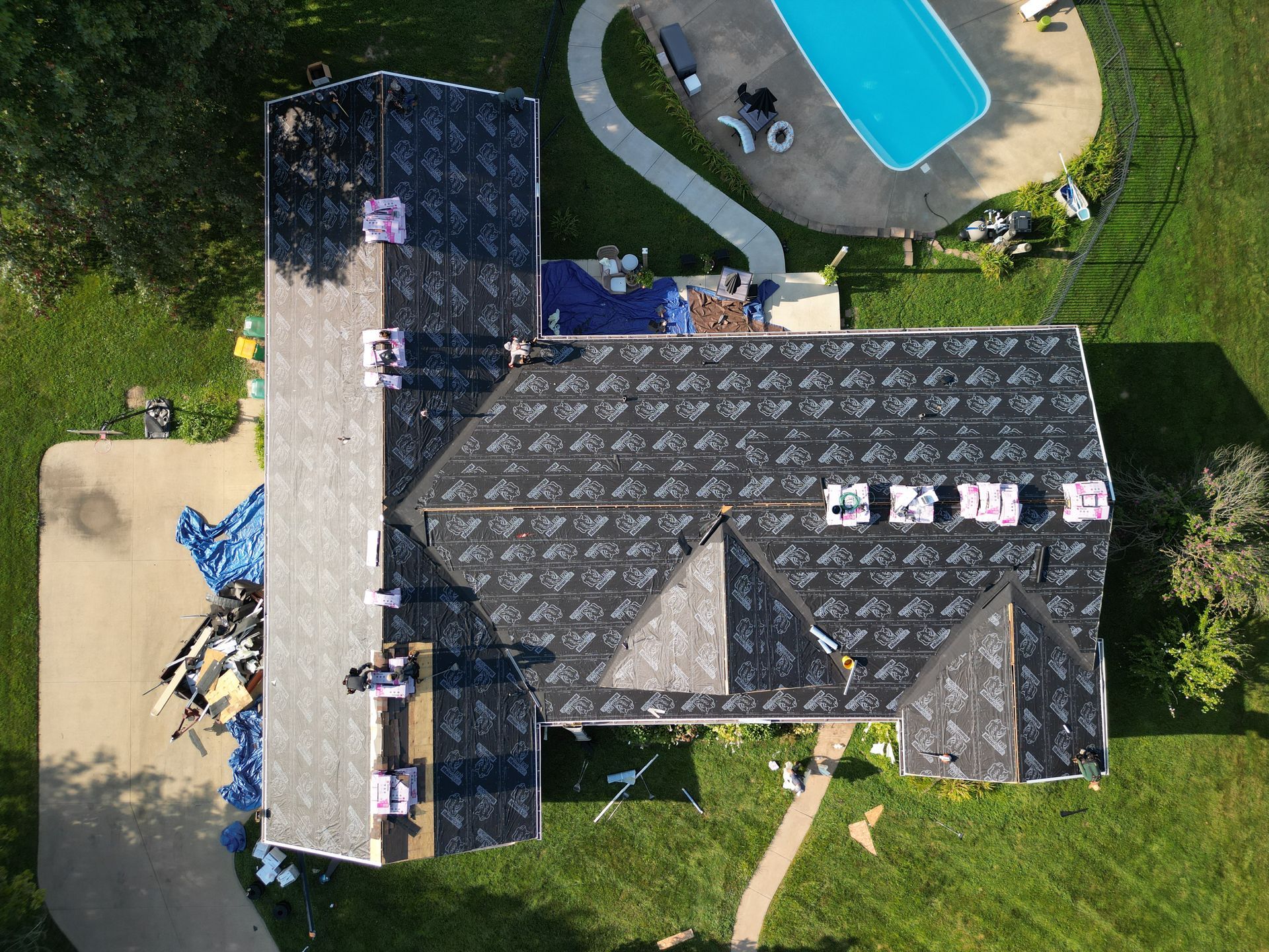 Aerial view of a house with dark roof, driveway, lawn, and a backyard pool.