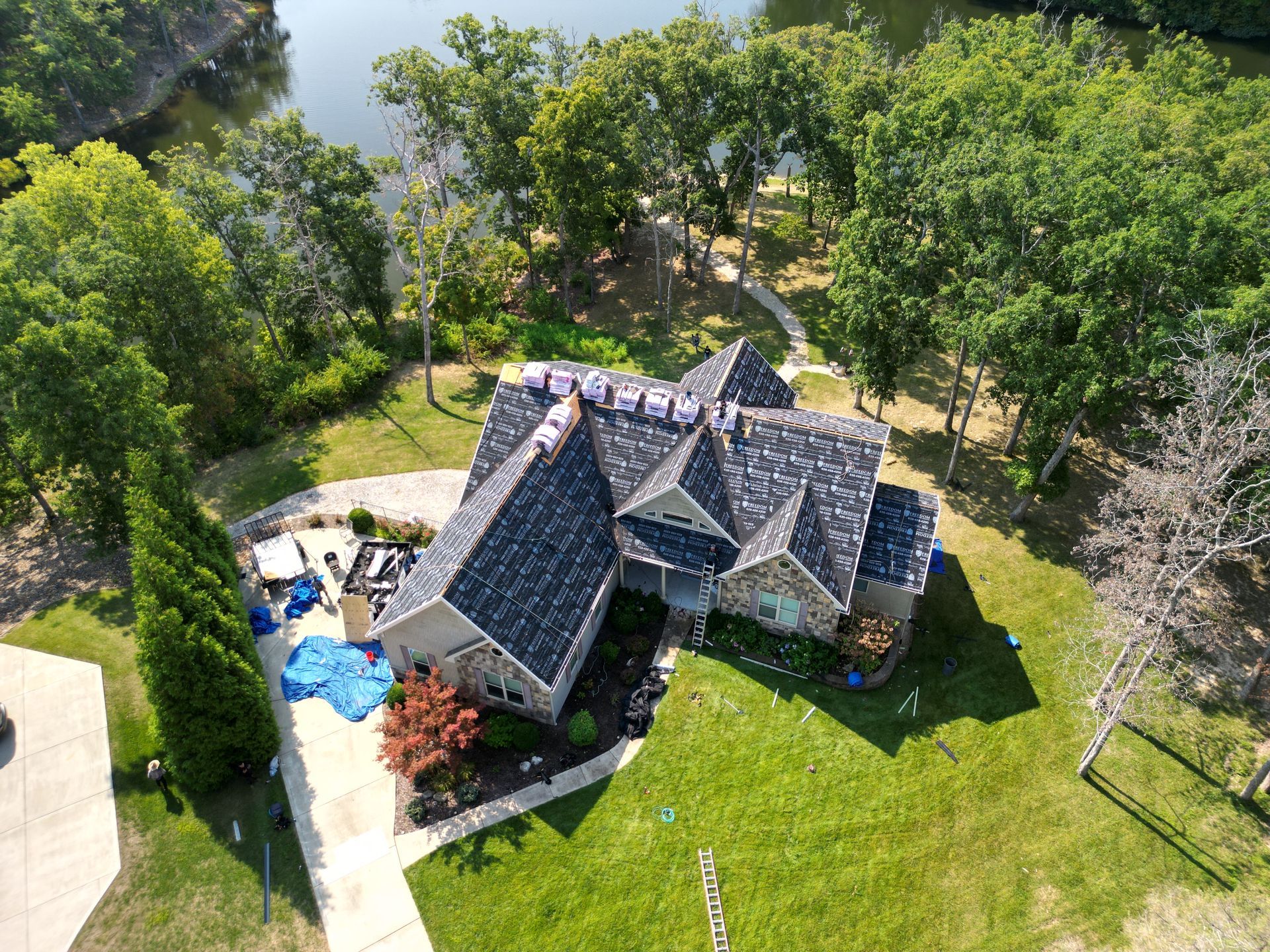 Aerial view of a house with a dark roof, green lawn, and surrounding trees in a wooded area