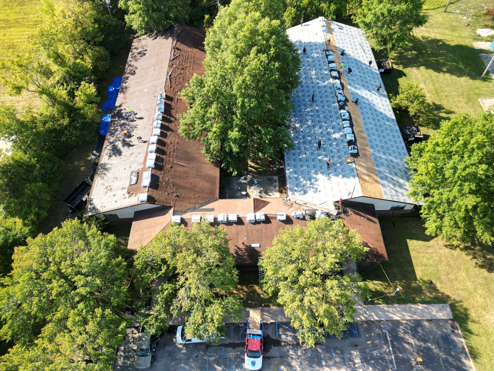 Aerial view of a house with brown and blue roofs surrounded by trees and a driveway