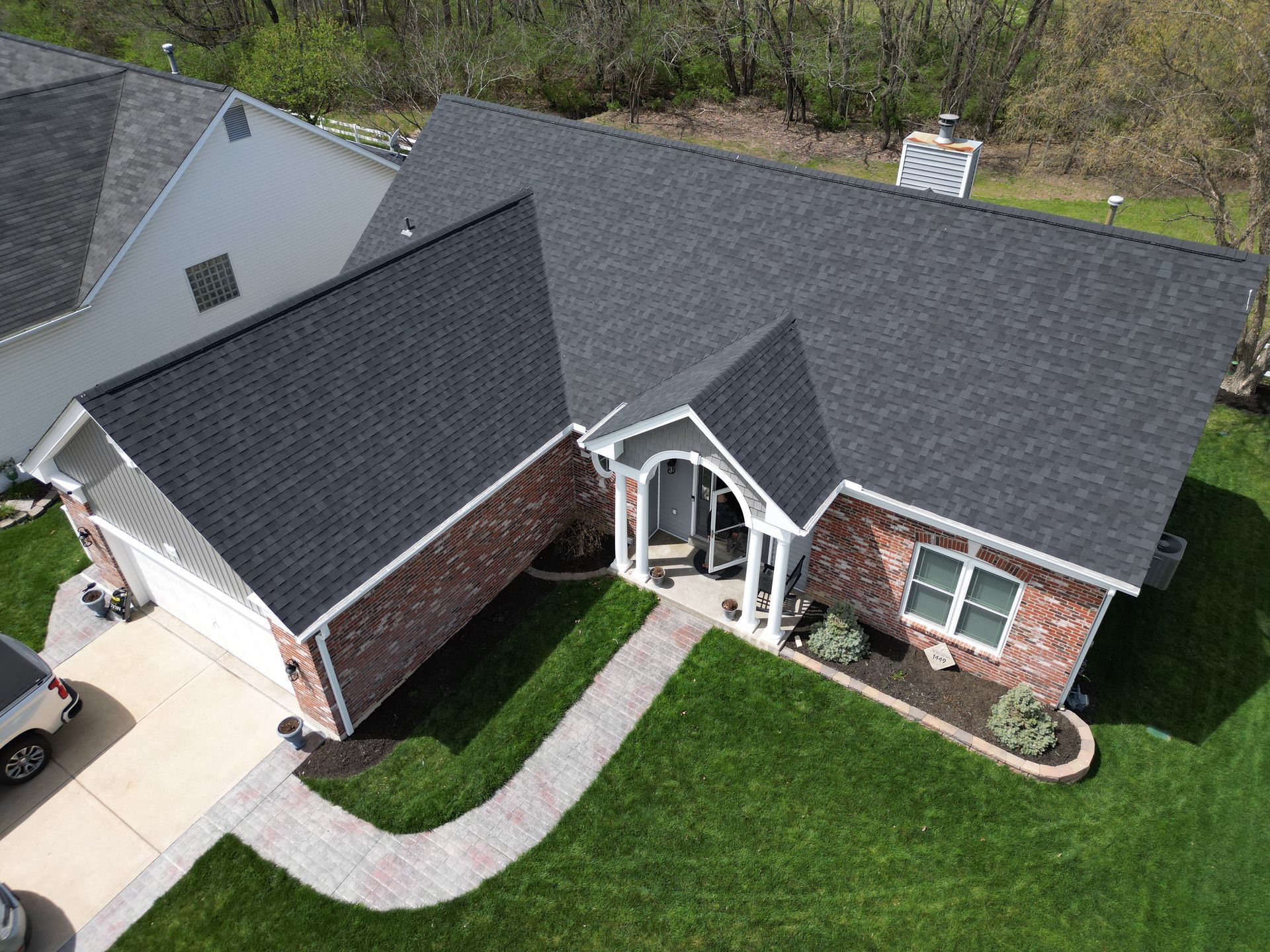 Aerial view of a brick house with dark gray roof, white entry, curved walkway, and green lawn.