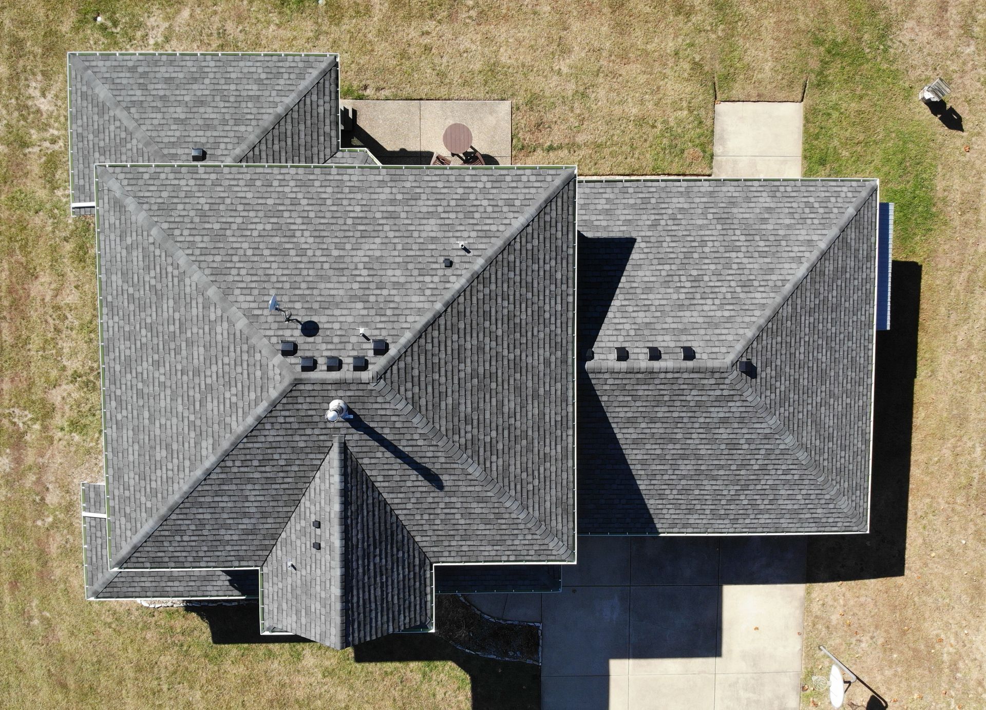 Aerial view of a gray-shingled house with a driveway and dry yard