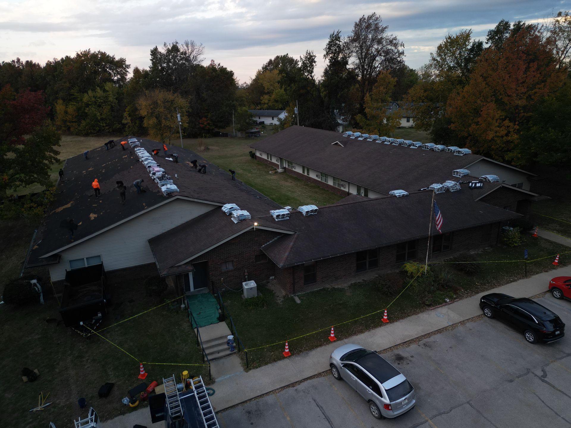 Aerial view of a house roof with workers and white tarps during roof repair, beside parked cars and trees