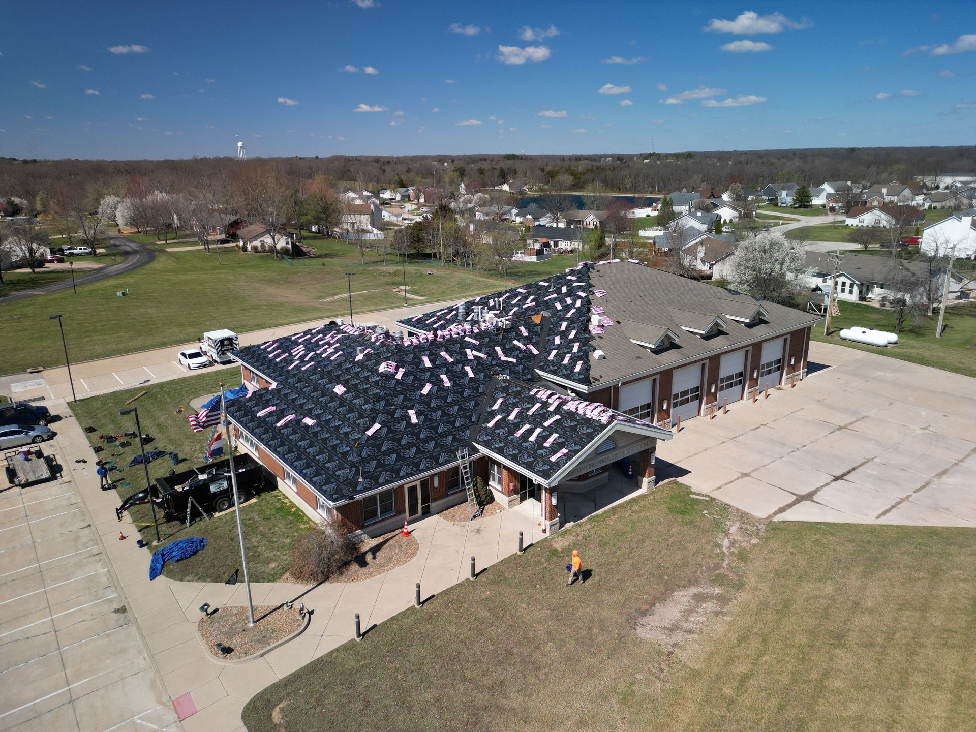 Aerial view of a building with a dark roof and an attached open pavilion in a suburban area.