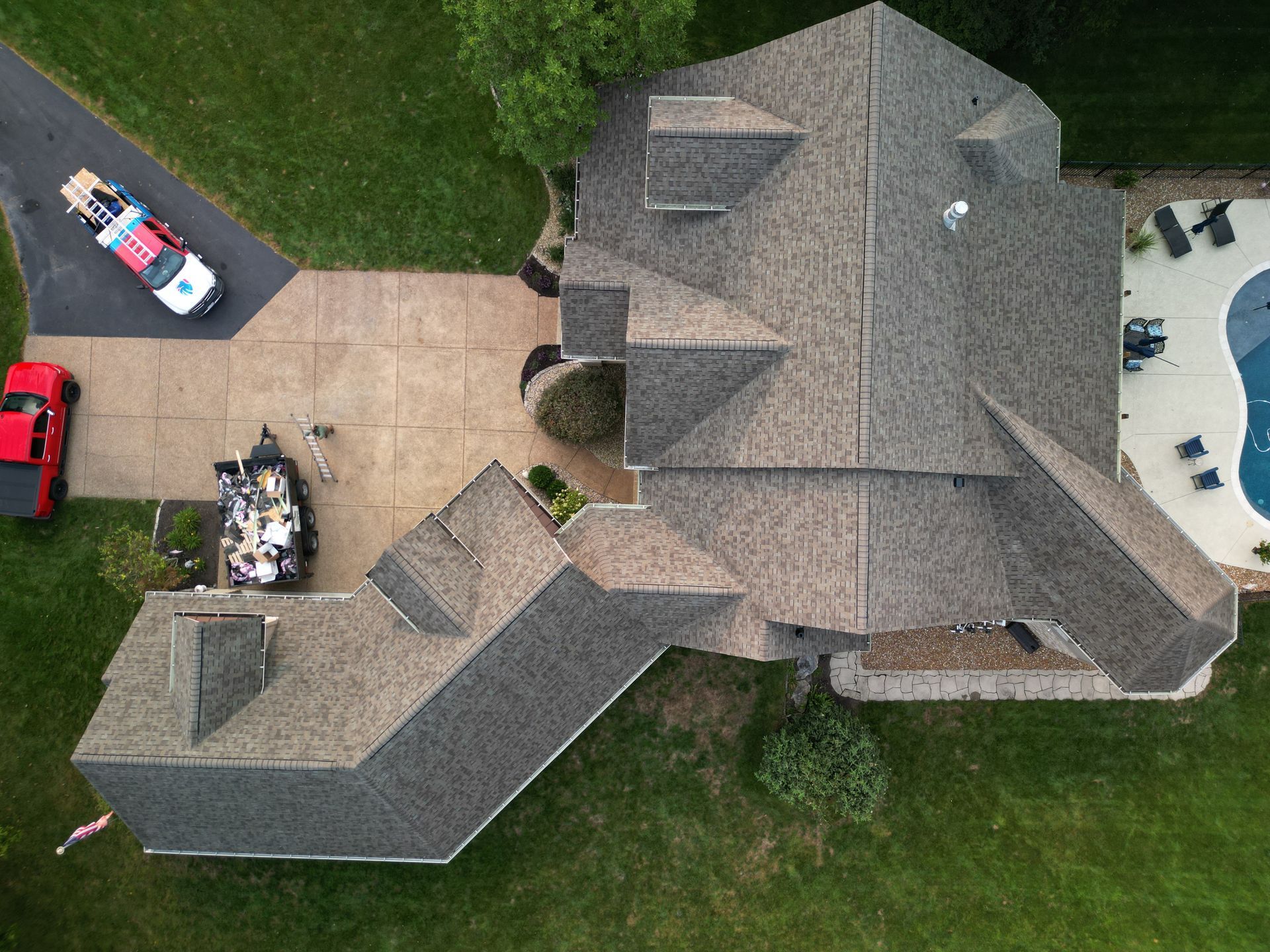 Aerial view of a large gray-roofed house with driveway, parked vehicles, and surrounding lawn.