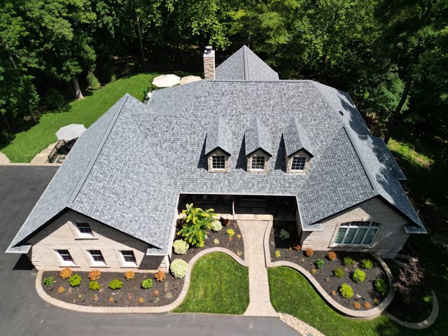 Aerial view of a gray-roofed house with a landscaped front yard and surrounding trees