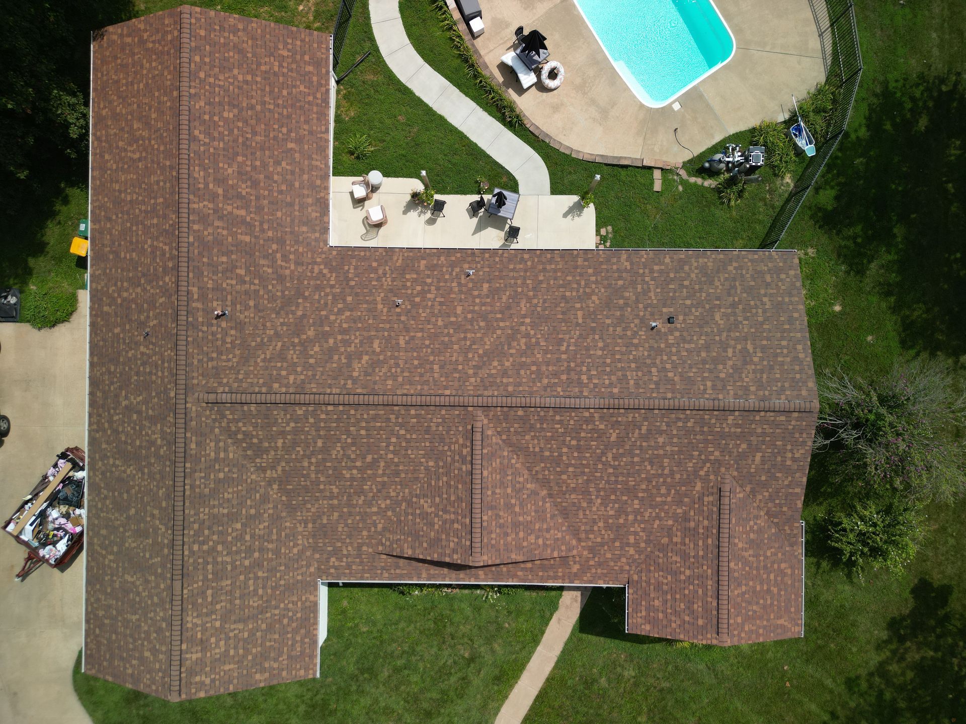 Aerial view of a brown-roofed house beside a backyard pool and patio.