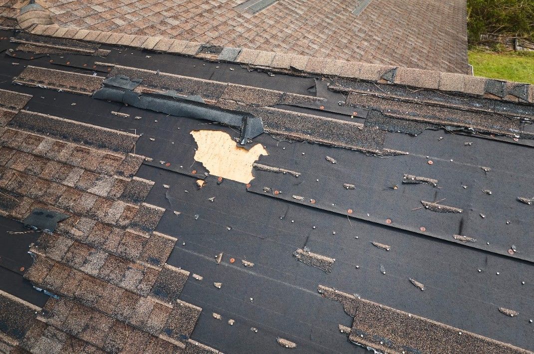 Damaged roof with missing shingles and exposed underlayment near the edge