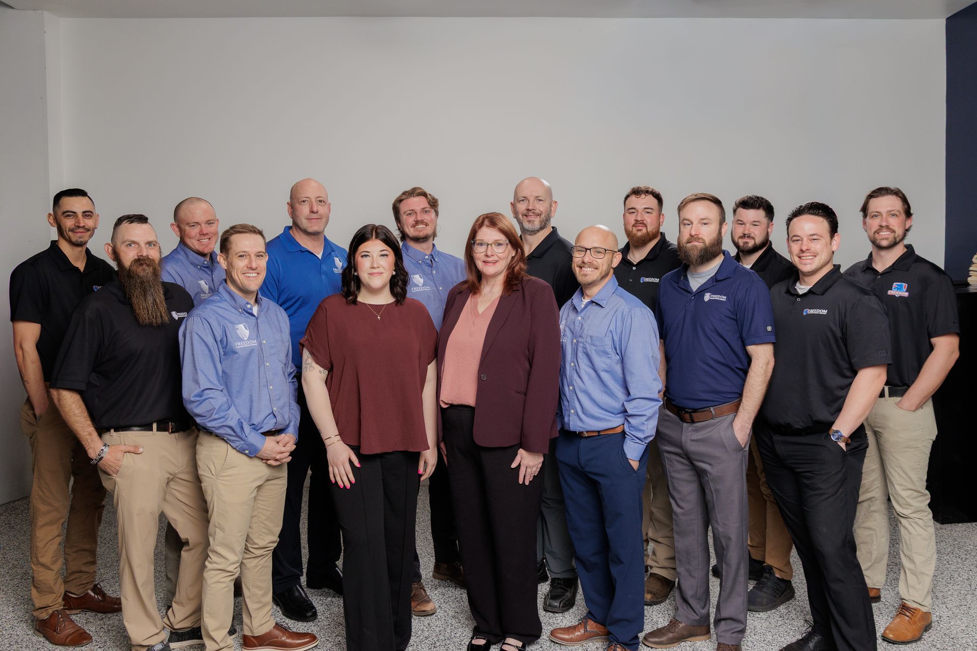 Group of employees posing indoors in business-casual attire against a plain white wall.
