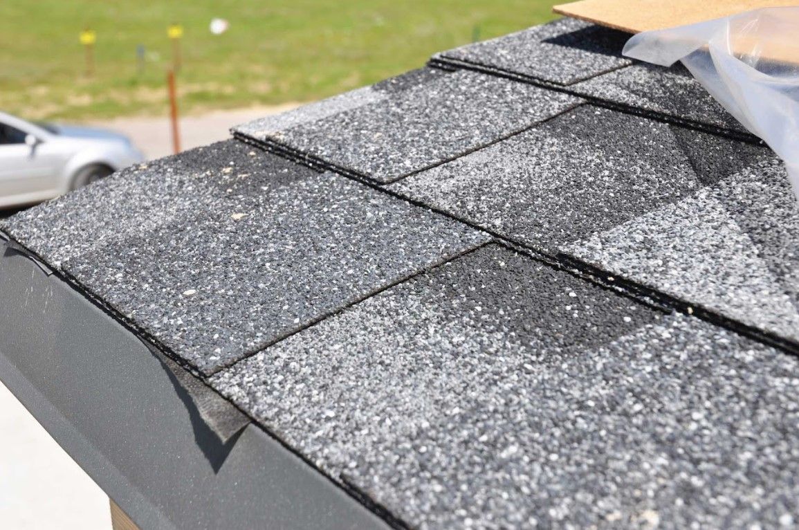 Close-up of a shingled roof with a small damaged patch near the edge