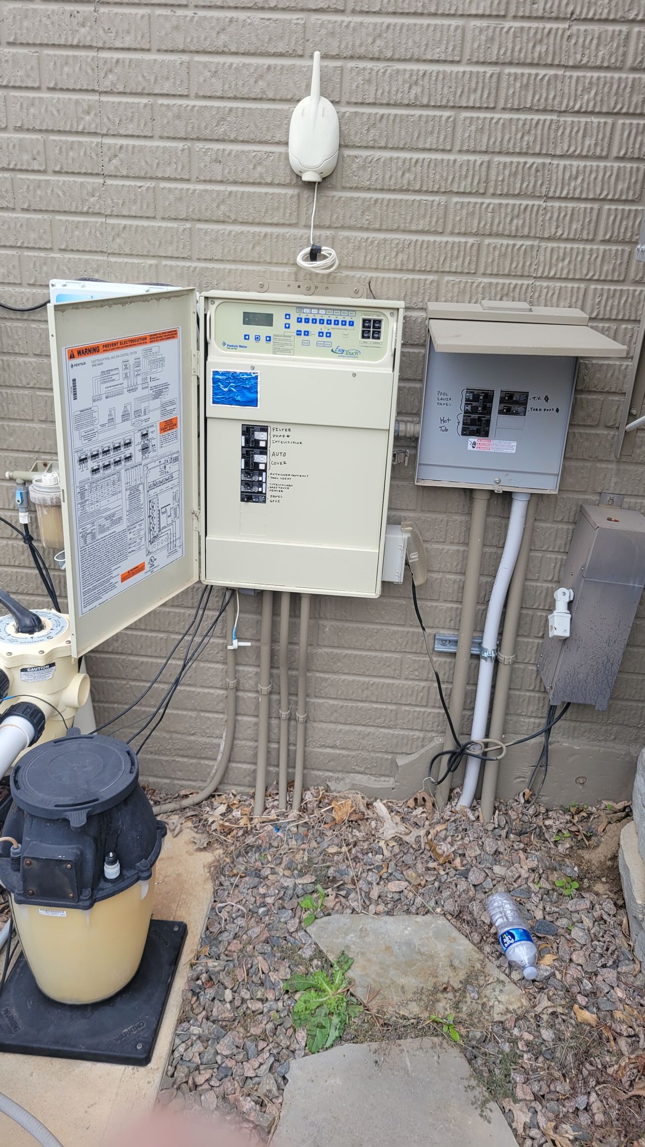A swimming pool controls box is sitting on the side of a brick wall.