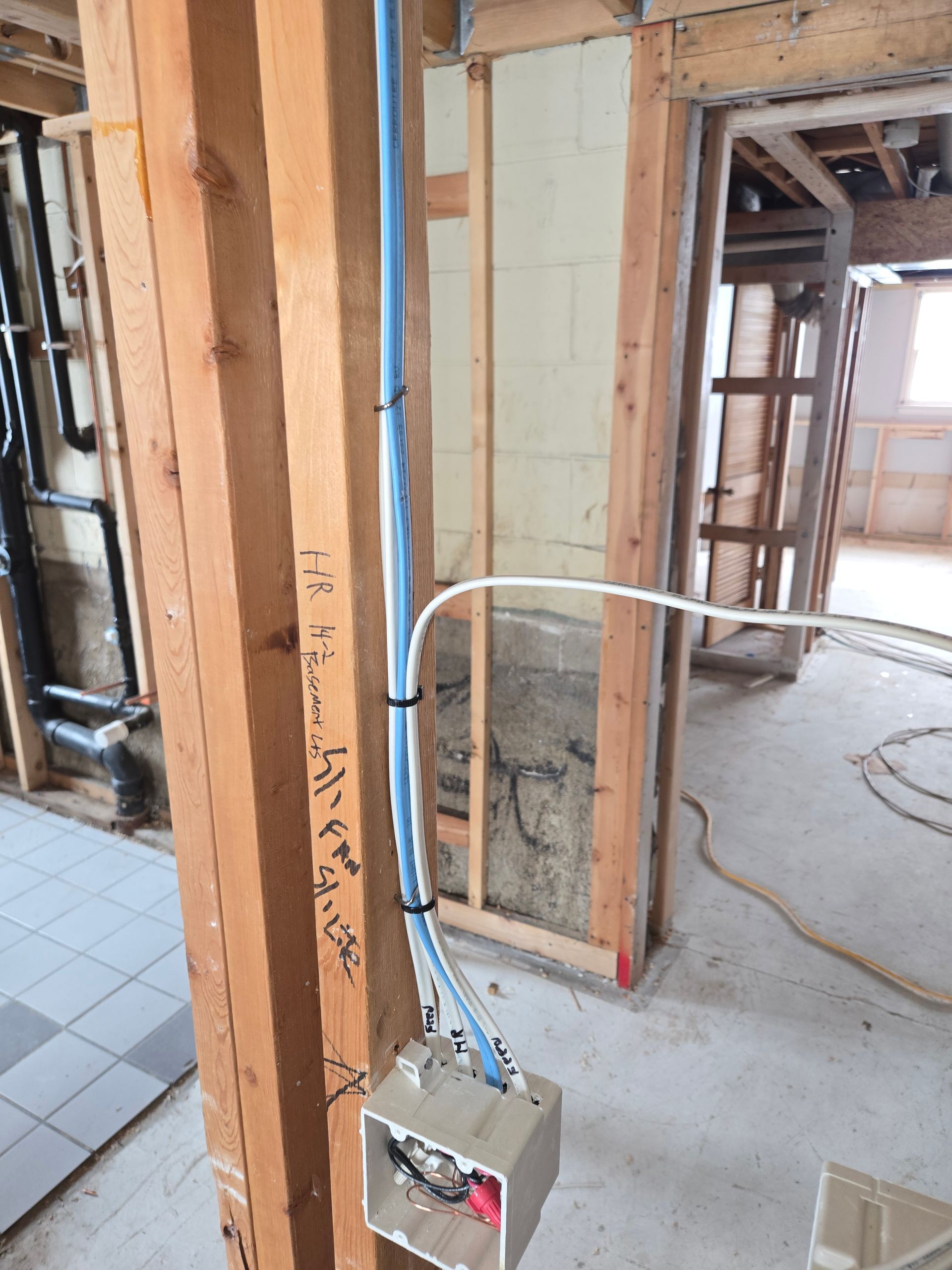 A box of wires is attached to a wooden post in a room under construction.