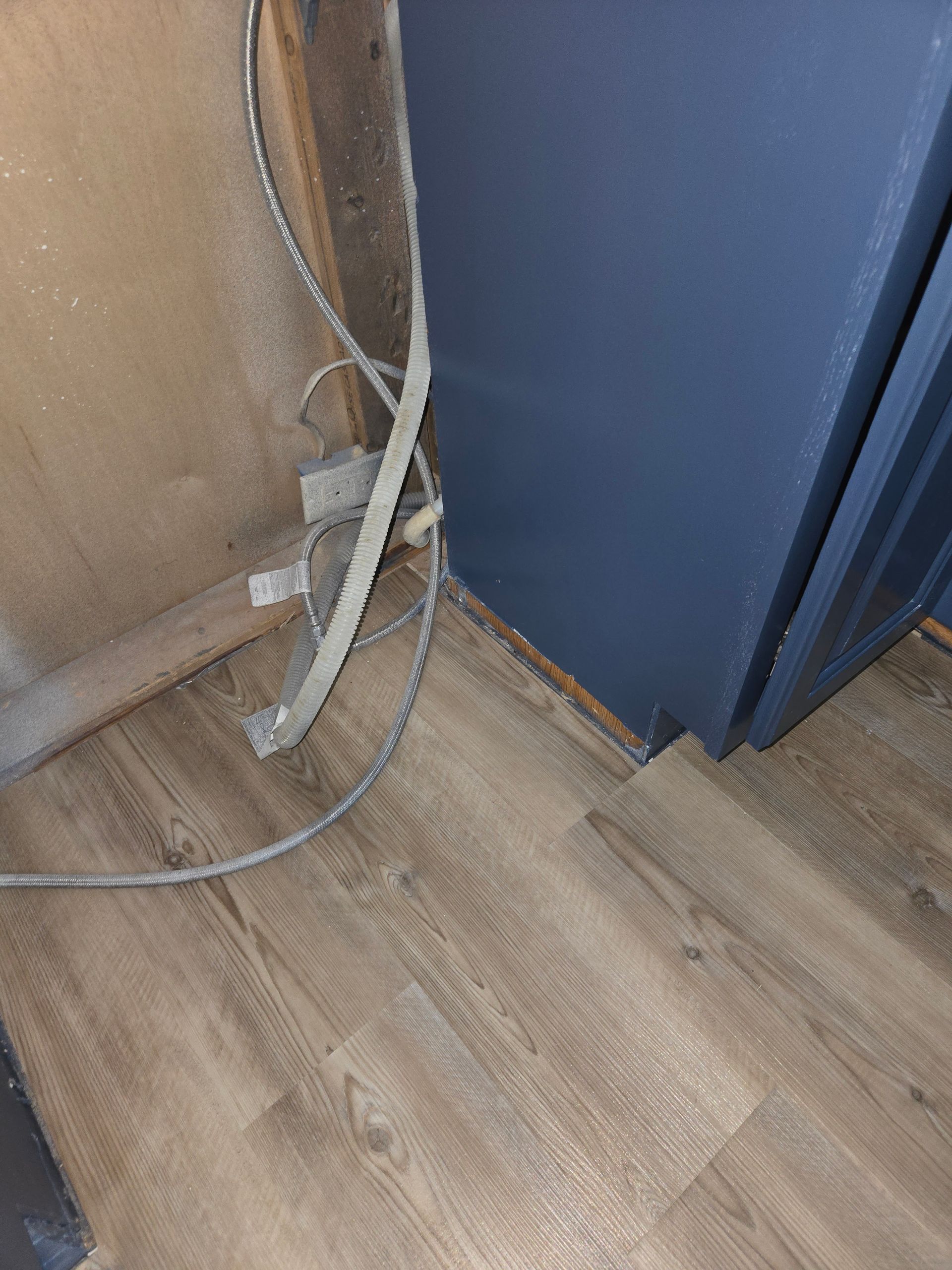 A blue refrigerator is sitting on a wooden floor next to a wall.