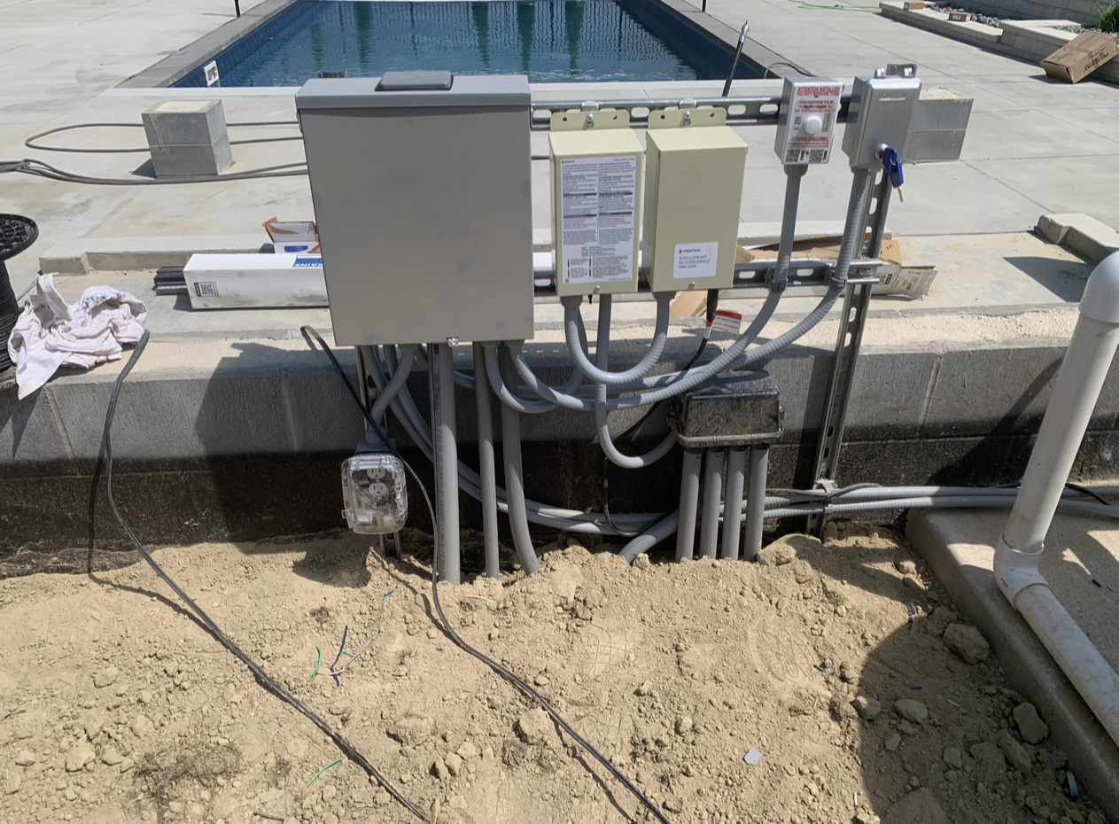 A electrical box is sitting in the dirt next to a pool.