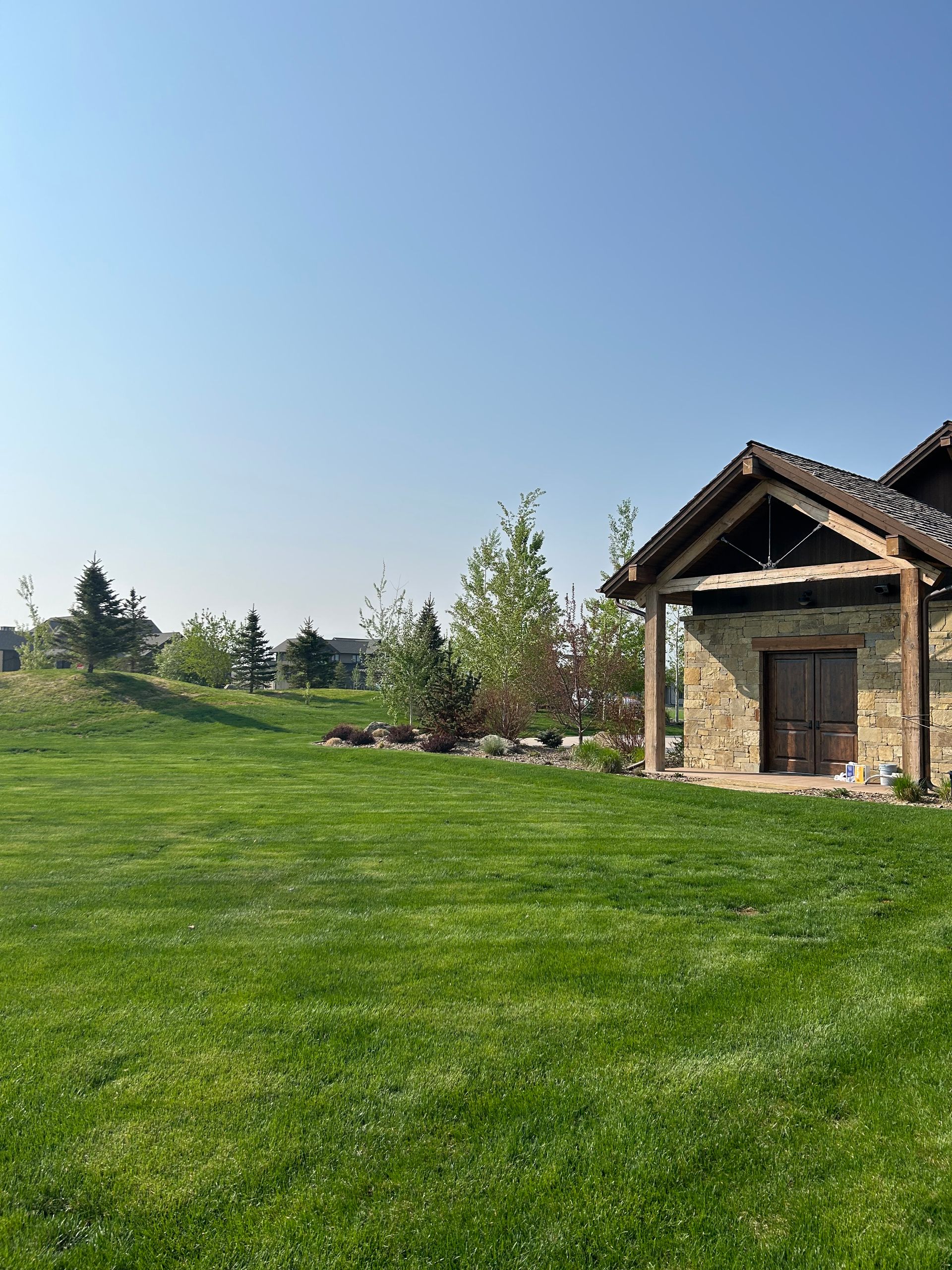 Stone cottage on a green lawn under a clear blue sky, with trees and shrubs in the background