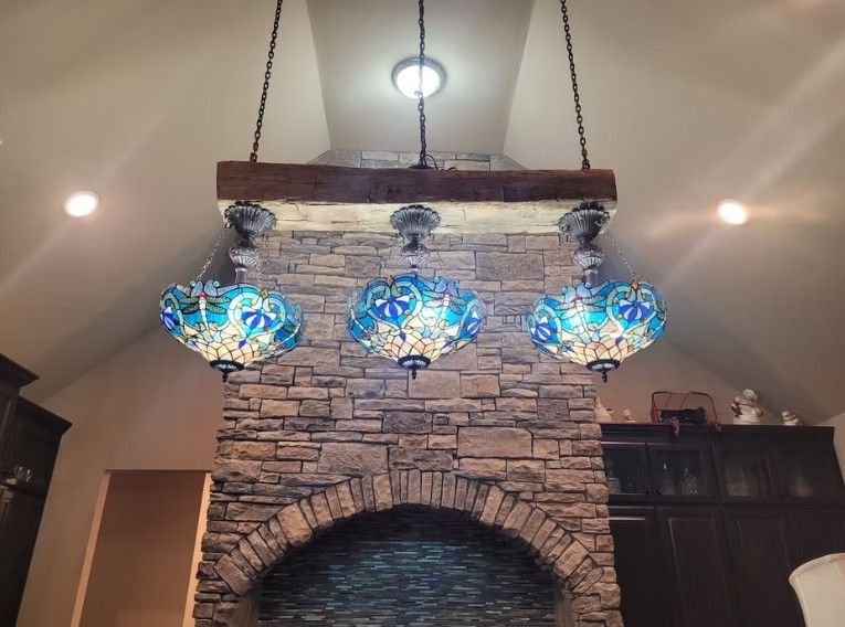 Three blue glass pendant lights hanging above a stone fireplace mantel