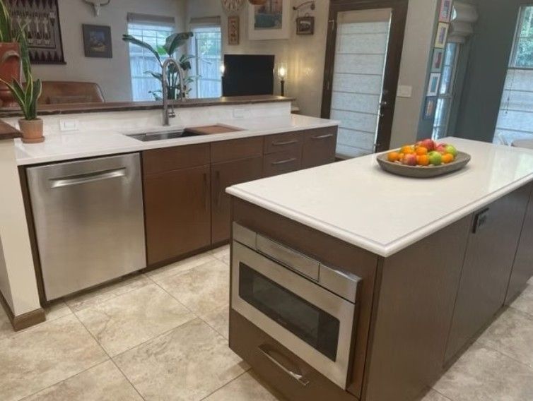 Modern kitchen with white island, stainless dishwasher and oven, brown cabinets, and fruit bowl on the counter