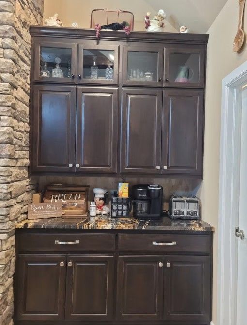 Dark wood kitchen cabinets with countertop appliances and stone wall accents in a home kitchen.