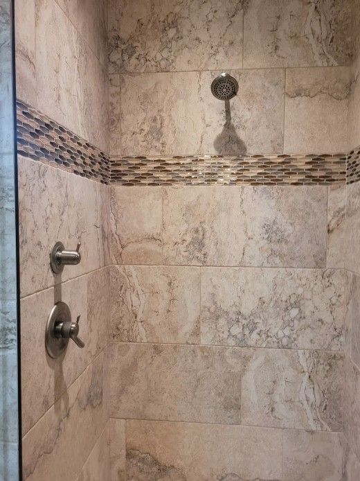 Tiled walk-in shower with chrome fixtures and decorative mosaic border.