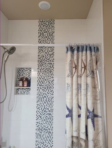 Bathroom shower with mosaic tile strip, wall shelf, and patterned curtain.