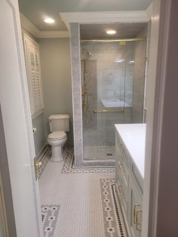 Narrow bathroom with walk-in glass shower, toilet, gray walls, and patterned tile floor
