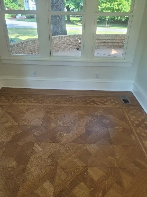 Empty room with parquet wood floor and large windows overlooking greenery