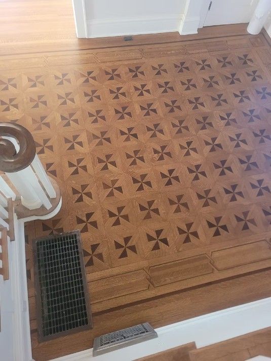 Patterned wooden floor landing with decorative inlay and two floor vents near a staircase.
