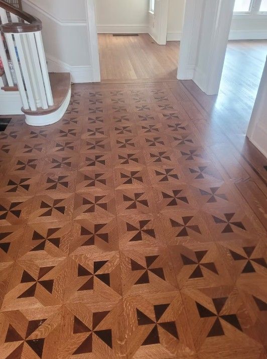Hallway with patterned wood floor leading into a bright room with white trim and stairs on the left