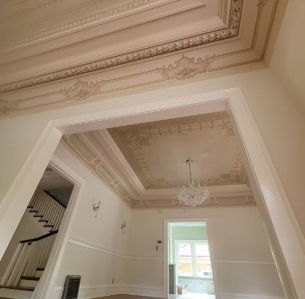 Ornate cream-colored interior ceiling and archway with decorative molding and a chandelier.