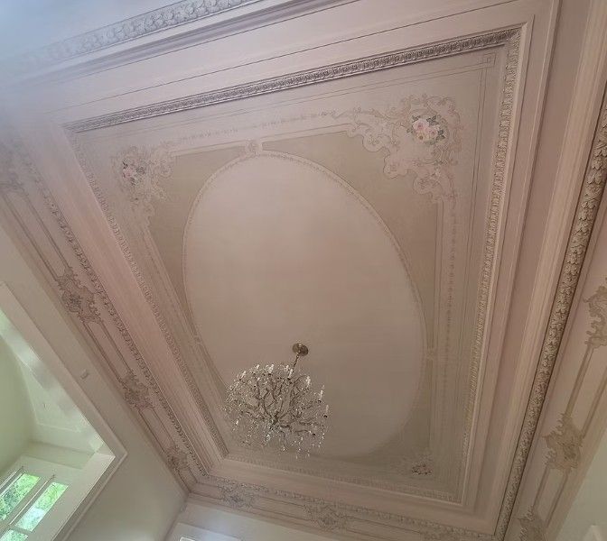 Ornate cream ceiling with decorative molding and a crystal chandelier, viewed upward.