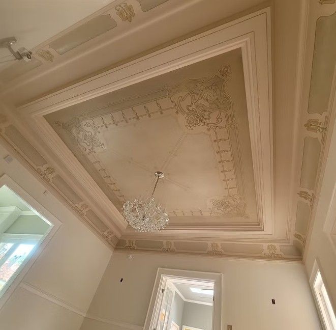 Ornate pastel ceiling with decorative molding, a chandelier, and two windows in a bright room