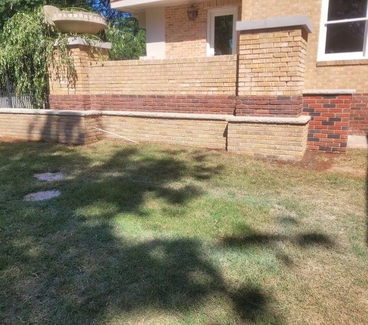 Brick house exterior with a low retaining wall and grassy front yard in sunlight