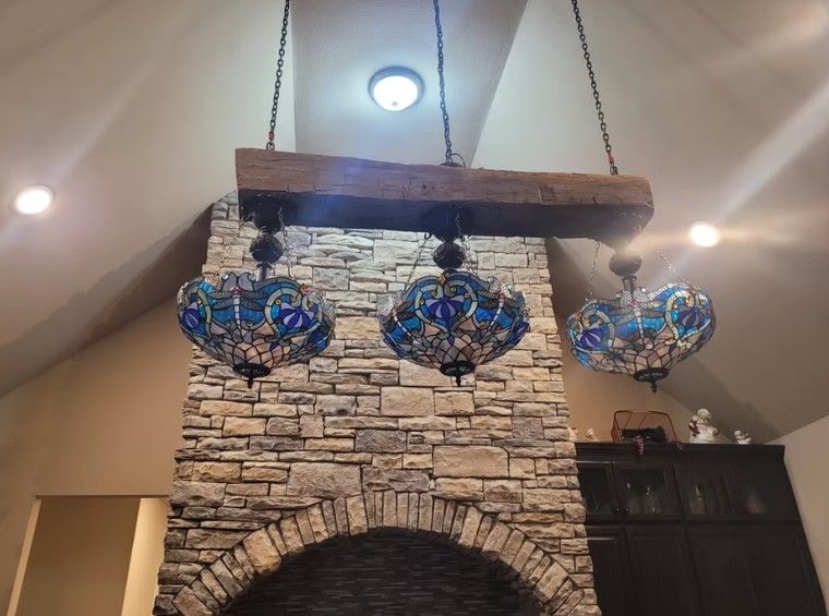 Three blue stained-glass pendant lights hang before a stone fireplace mantel.